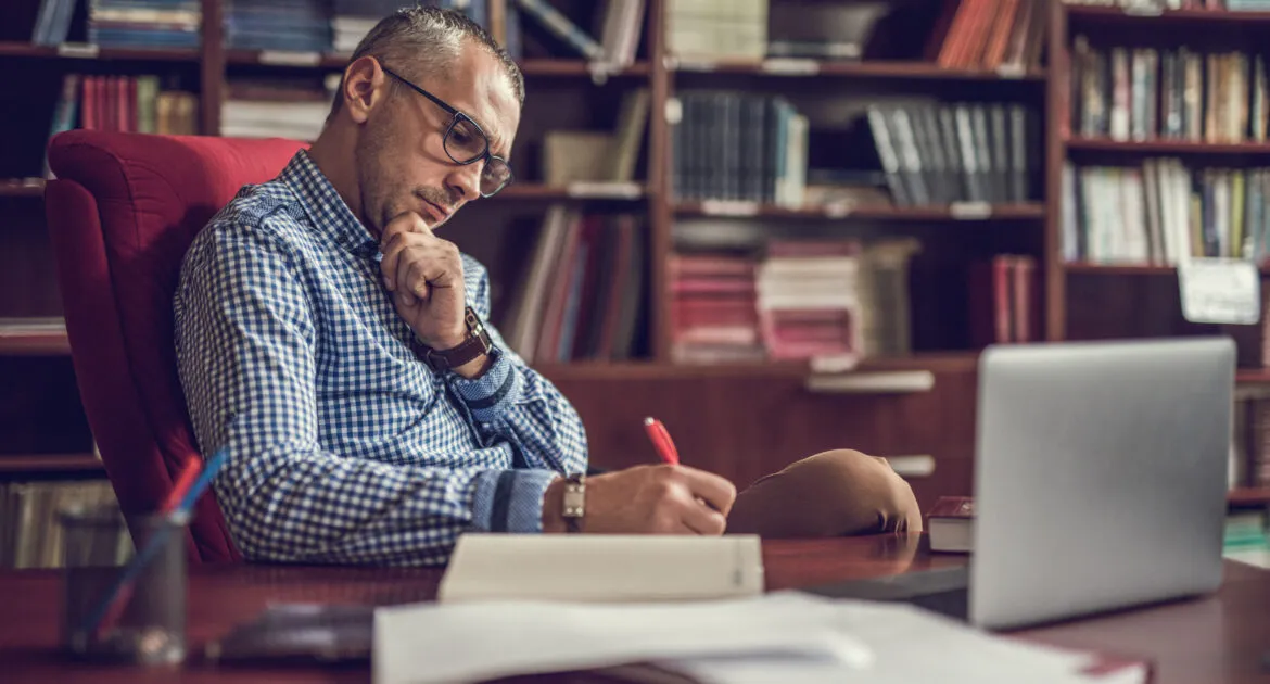 Male lecturer taking notes in home office.