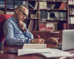 Male lecturer taking notes in home office.