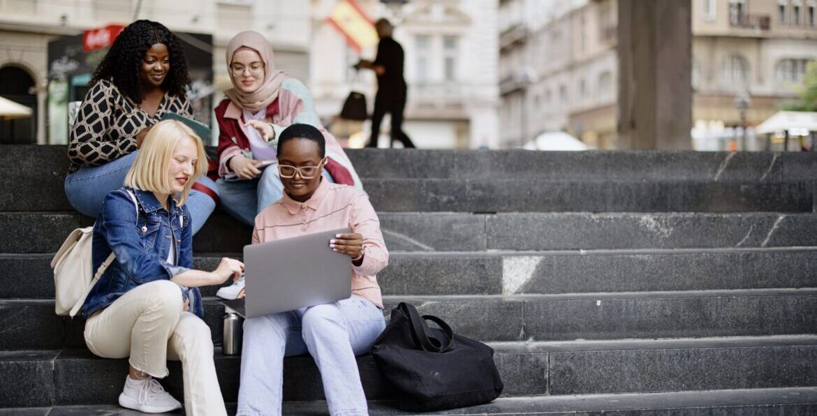 Students sit on the steps near the college and look at the laptop and digital tablet and talk