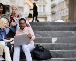 Students sit on the steps near the college and look at the laptop and digital tablet and talk