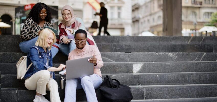 Students sit on the steps near the college and look at the laptop and digital tablet and talk