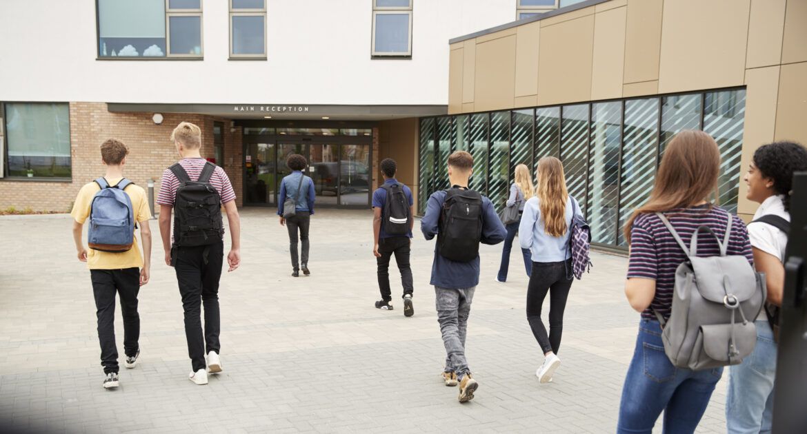 Rear View Of College Students Walking Into College Building Together