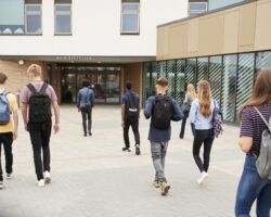 Rear View Of College Students Walking Into College Building Together