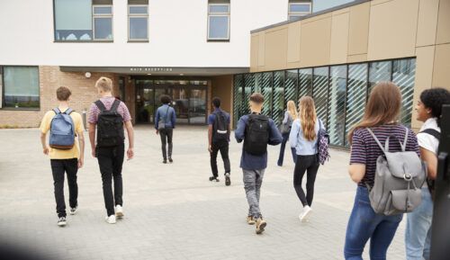 Rear View Of College Students Walking Into College Building Together