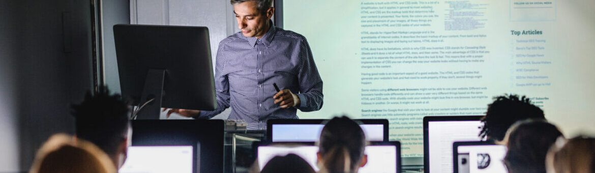 Mid adult professor teaching a lecture from desktop PC at computer lab.