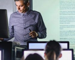 Mid adult professor teaching a lecture from desktop PC at computer lab.