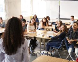 Rear View Of Female Further Education Teacher Standing At Front Of Class giving a revision lesson