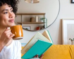 Pensive relaxed woman reading a book at home, drinking coffee sitting on the couch for teacher wellbeing.