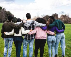 Group of six teenager friends embracing together at the park, rear view