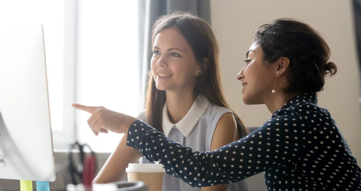 Female intern listening to mentor explaining computer task