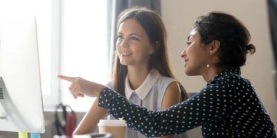Female intern listening to mentor explaining computer task