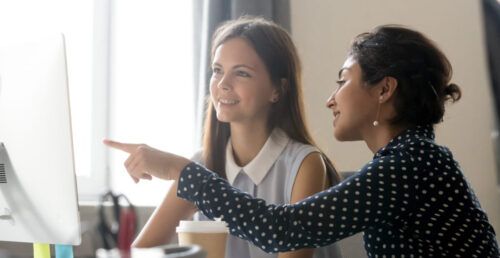 Female intern listening to mentor explaining computer task