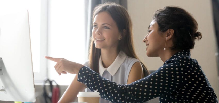 Female intern listening to mentor explaining computer task