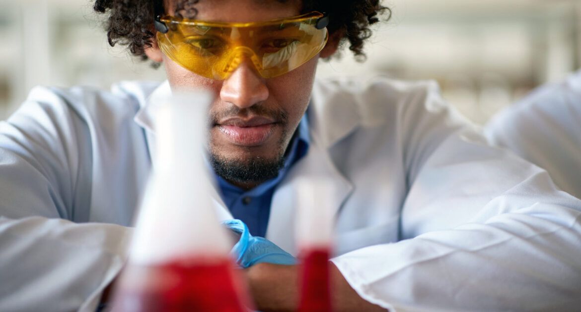 A young male chemistry student observes a chemical in a test tube in the laboratory.