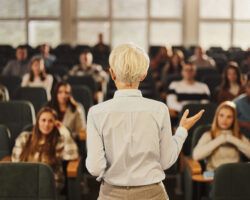 Back view of a female professor teaching her students at lecture hall.