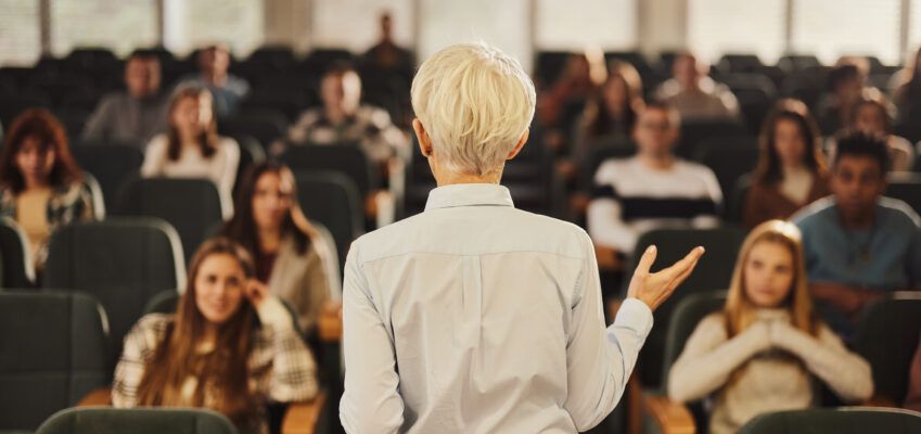 Back view of a female professor teaching her students at lecture hall.