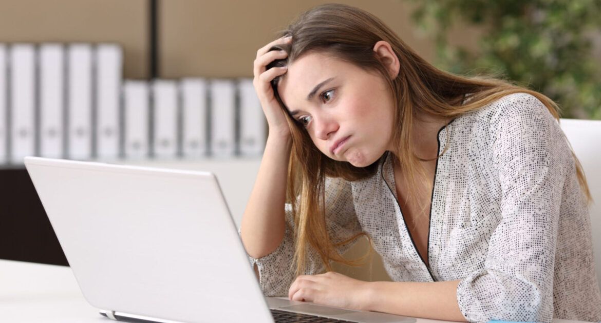 Woman sat at laptop looking disappointed at another application rejection