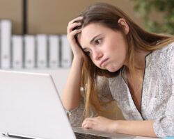 Woman sat at laptop looking disappointed at another application rejection