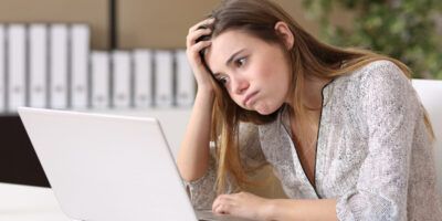 Woman sat at laptop looking disappointed at another application rejection