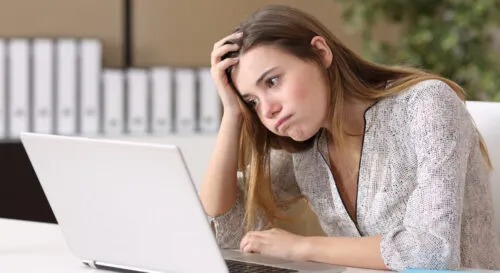 Woman sat at laptop looking disappointed at another application rejection