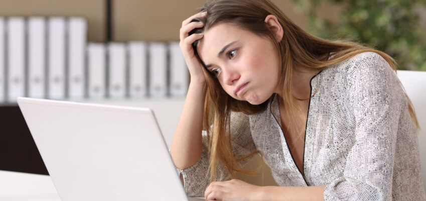 Woman sat at laptop looking disappointed at another application rejection