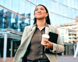 Confident Businesswoman Walking with Coffee Outside Modern Office Building