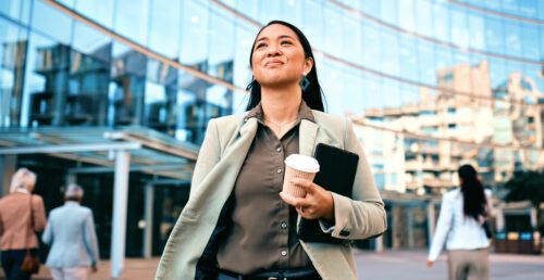 Confident Businesswoman Walking with Coffee Outside Modern Office Building