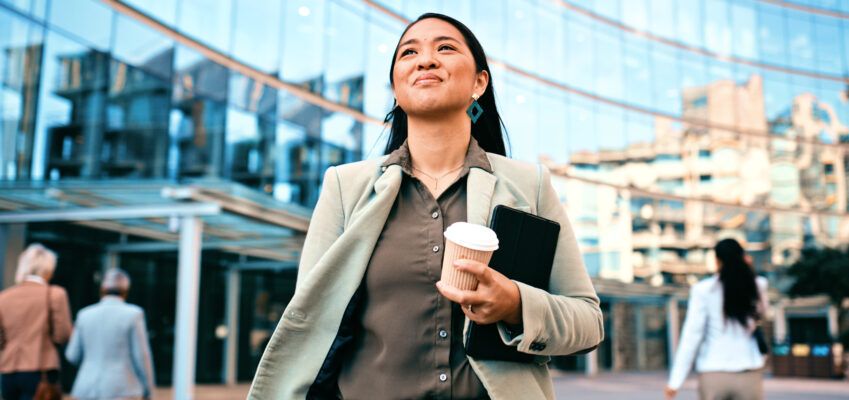 Confident Businesswoman Walking with Coffee Outside Modern Office Building