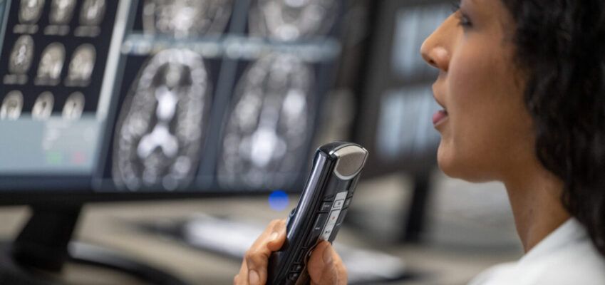 Female radiologist speaking into a dictation recorder while looking at MRI scan