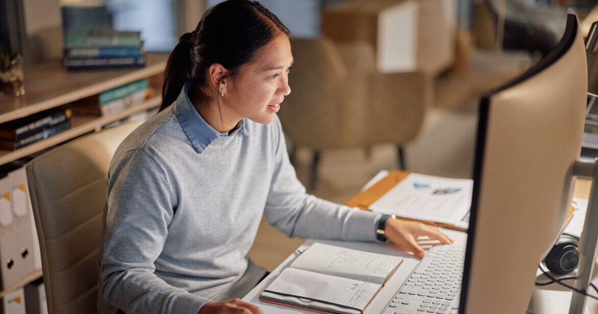 Woman sat at computer writing a PhD research proposal.