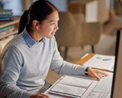 Woman sat at computer writing a PhD research proposal.