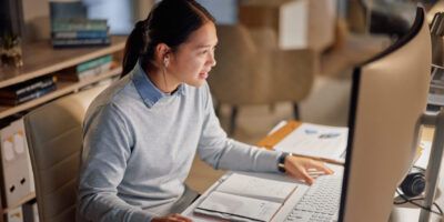 Woman sat at computer writing a PhD research proposal.