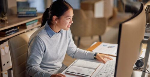 Woman sat at computer writing a PhD research proposal.