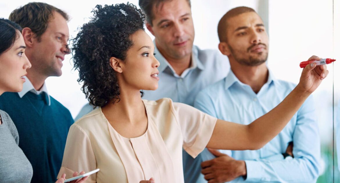 Business people, writing and coaching with tablet for planning, tasks or agenda on glass board at office. Group of young and creative employees taking notes for discussion, brainstorming or startup