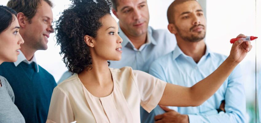 Business people, writing and coaching with tablet for planning, tasks or agenda on glass board at office. Group of young and creative employees taking notes for discussion, brainstorming or startup