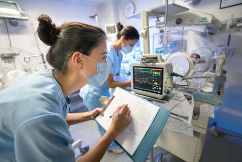 Nurse monitoring a premature newborn in an incubator while wearing a facemask