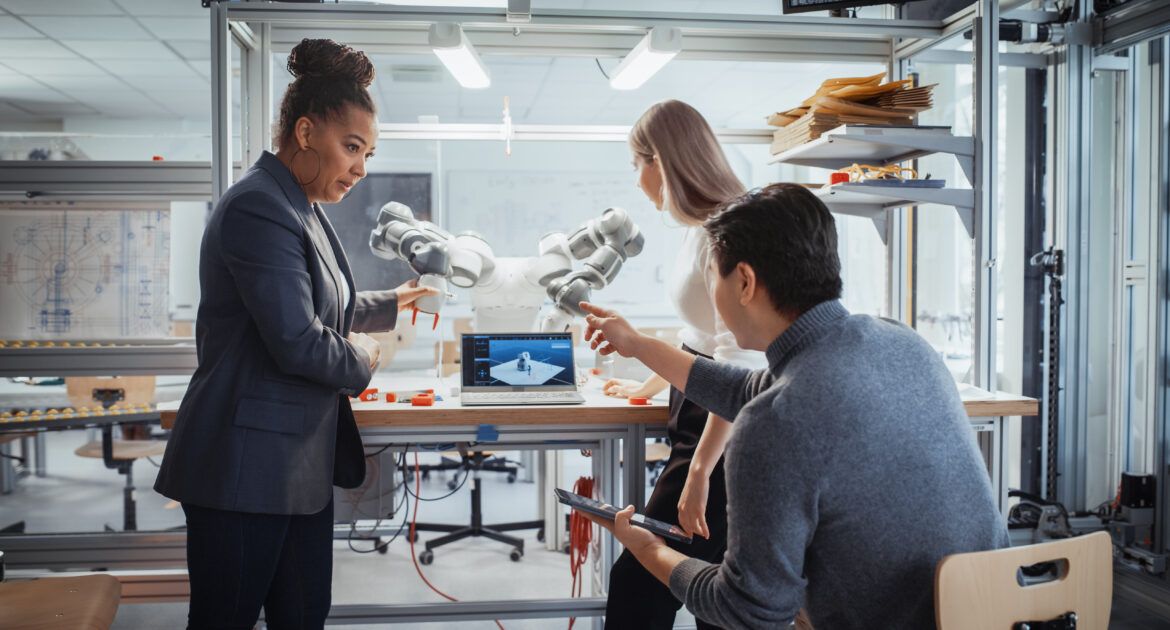 Diverse Team of Future Robotics Engineers Working on Robot Arm Design for their research careers Under the Supervision of Black Professor. Digital Technology and Intelligent Students Concept.