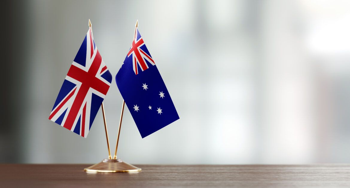 Australian And British Flag Pair On A Desk Over Defocused Background