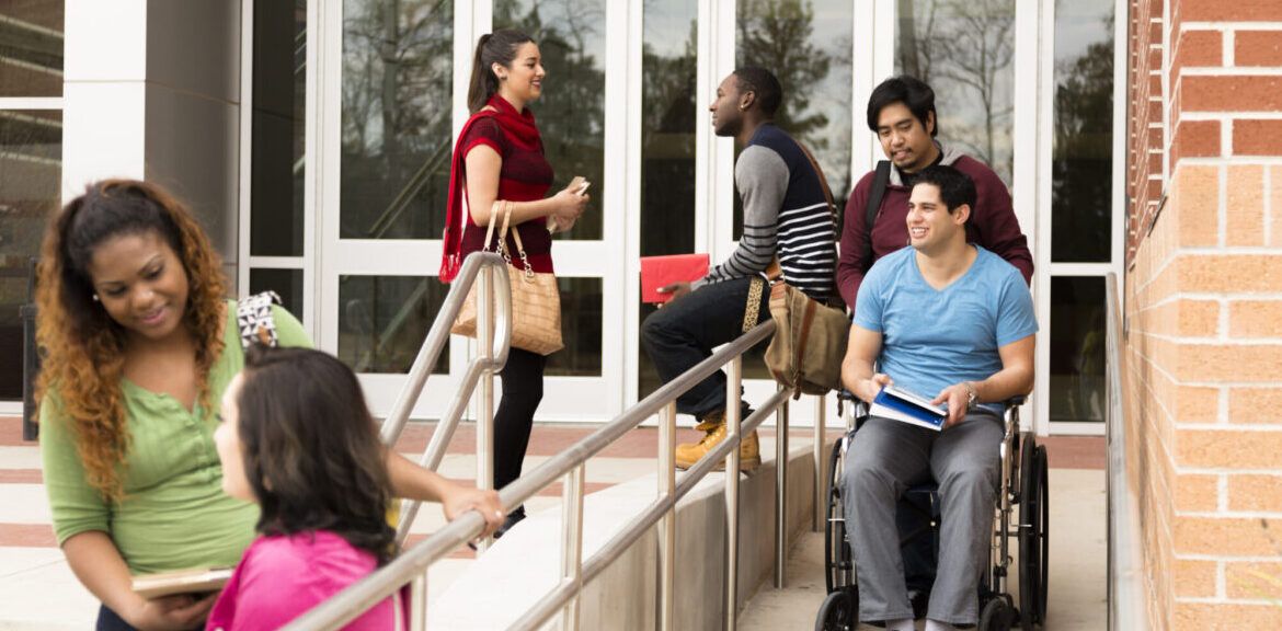 Education: Disabled student helped down wheelchair ramp. College campus.