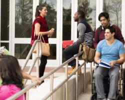 Education: Disabled student helped down wheelchair ramp. College campus.