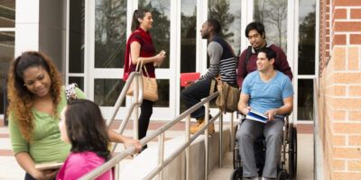 Education: Disabled student helped down wheelchair ramp. College campus.