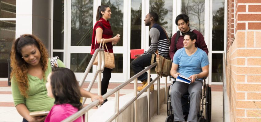 Education: Disabled student helped down wheelchair ramp. College campus.