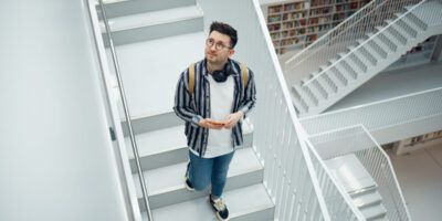 Library search, geek student or intelligent man for phd research, creative vision and knowledge in university. College, stairs above and person thinking of books for education, scholarship or study