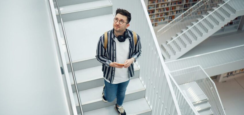 Library search, geek student or intelligent man for phd research, creative vision and knowledge in university. College, stairs above and person thinking of books for education, scholarship or study