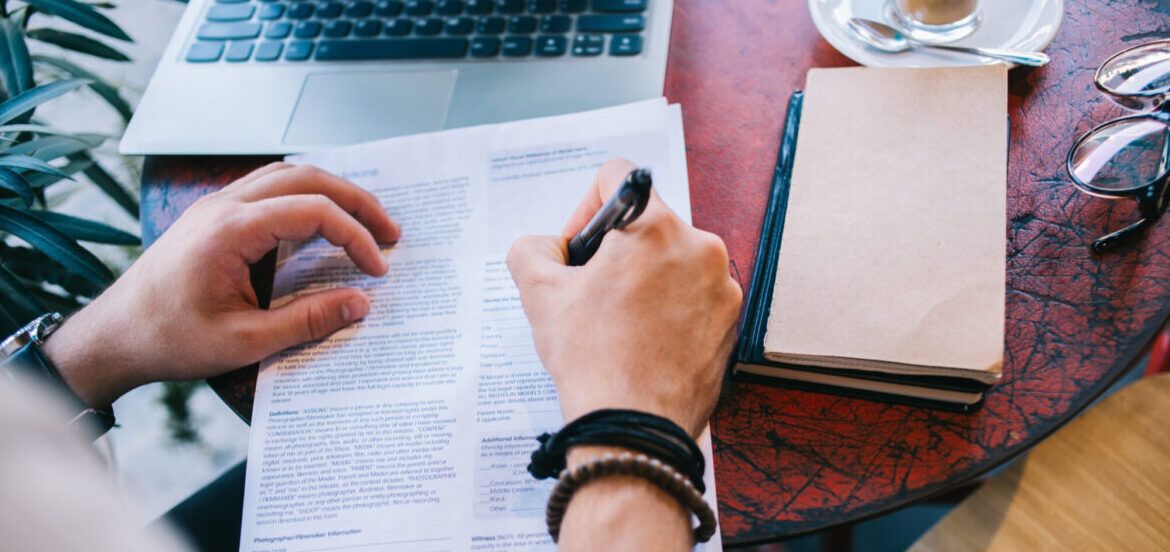 Top view of male writing a cv with questionnaire applying for job offer sitting at working place with notebook and laptop, cropped image of male fill in application form