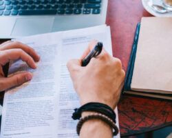 Top view of male writing a cv with questionnaire applying for job offer sitting at working place with notebook and laptop, cropped image of male fill in application form