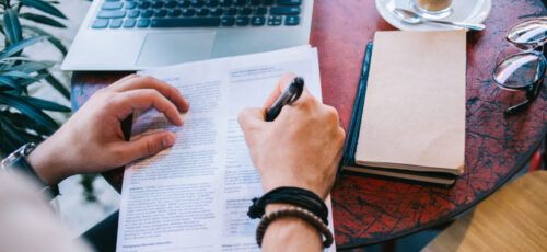 Top view of male writing a cv with questionnaire applying for job offer sitting at working place with notebook and laptop, cropped image of male fill in application form